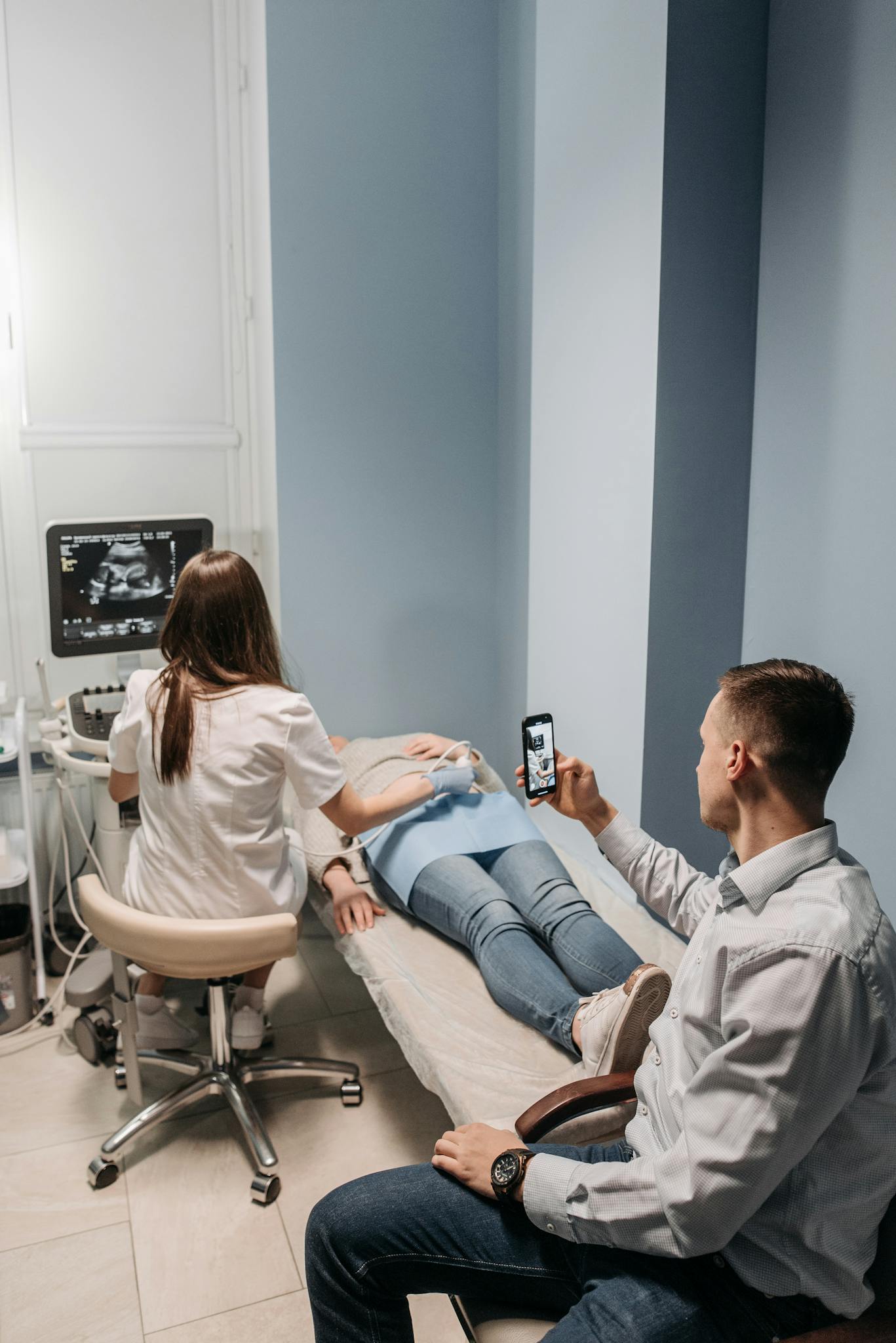 A woman receives an ultrasound as her partner watches and records the session on a smartphone.